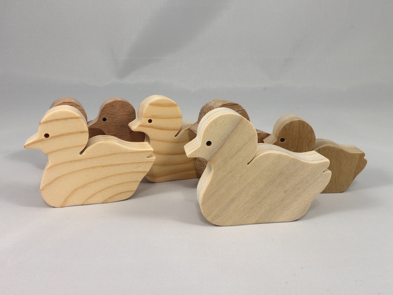 Five wooden duck figurines in various shades of brown and beige. The ducks are all facing the same direction and are arranged in a row.