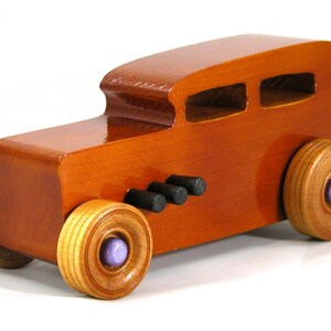 This is a handmade wooden toy car modeled after a Hot Rod 1932 Ford Sedan. It is made from wood, finished with multiple coats of amber shellac, and trimmed with black and metallic purple acrylic paint.