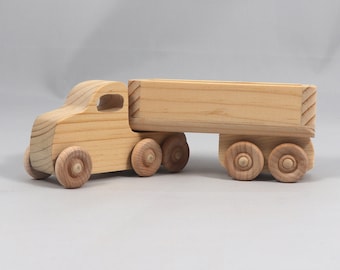 May include: A wooden toy truck with a flatbed trailer. The truck and trailer are both unpainted and have four wheels each.