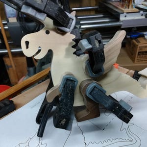 Wooden baby dragon figurine held with multiple clamps while its contrasting wood wings, ears, arms, and legs are glued in place.