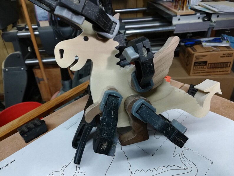 Wooden baby dragon figurine held with multiple clamps while its contrasting wood wings, ears, arms, and legs are glued in place.