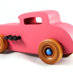 This is a handmade wooden Hot Rod '32 Deuce Coupe toy car. It is hand-painted hot pink with black and metallic sapphire blue trim. The hardwood wheels are finished with nonmarring amber shellac.