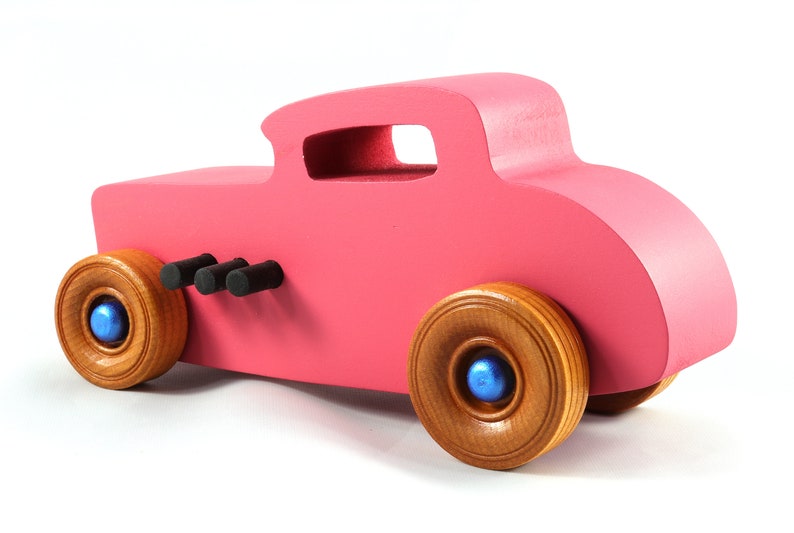 This is a handmade wooden Hot Rod '32 Deuce Coupe toy car. It is hand-painted hot pink with black and metallic sapphire blue trim. The hardwood wheels are finished with nonmarring amber shellac.