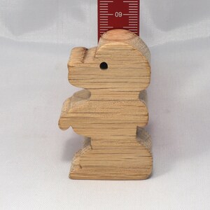 May include: A wooden toy shaped like a standing bear. The bear is light brown and has a hole in its head. The bear is about 4 inches tall.
