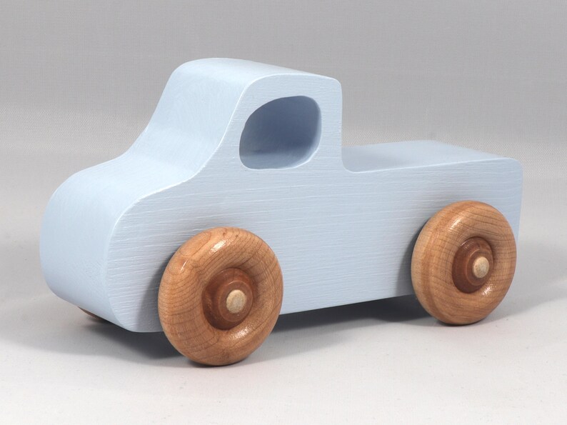 May include: A light blue wooden toy truck with natural wood wheels. The truck has a classic pickup design with a cab and a cargo bed. The wheels are round and attached to the truck's body. A simple and charming toy.