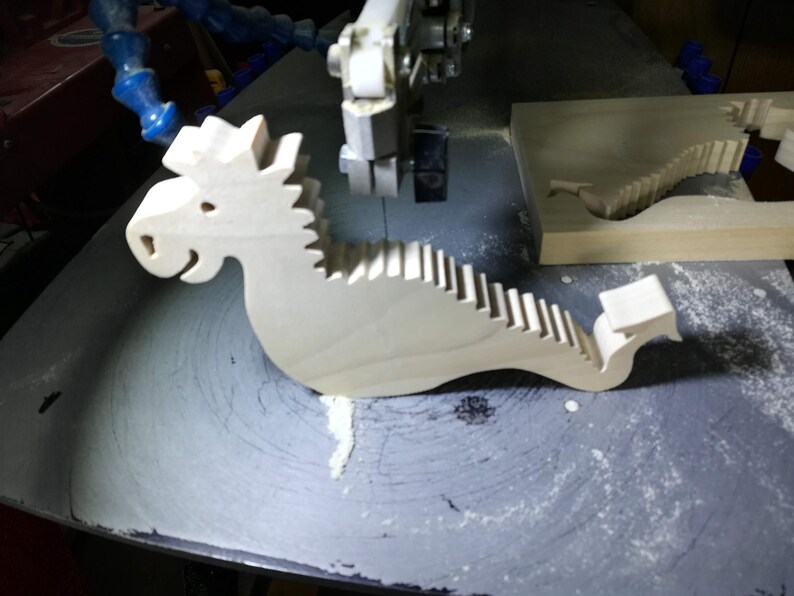 Freshly cut wooden baby dragon body resting on a scroll saw table beside the remaining hardwood blank and sawdust.