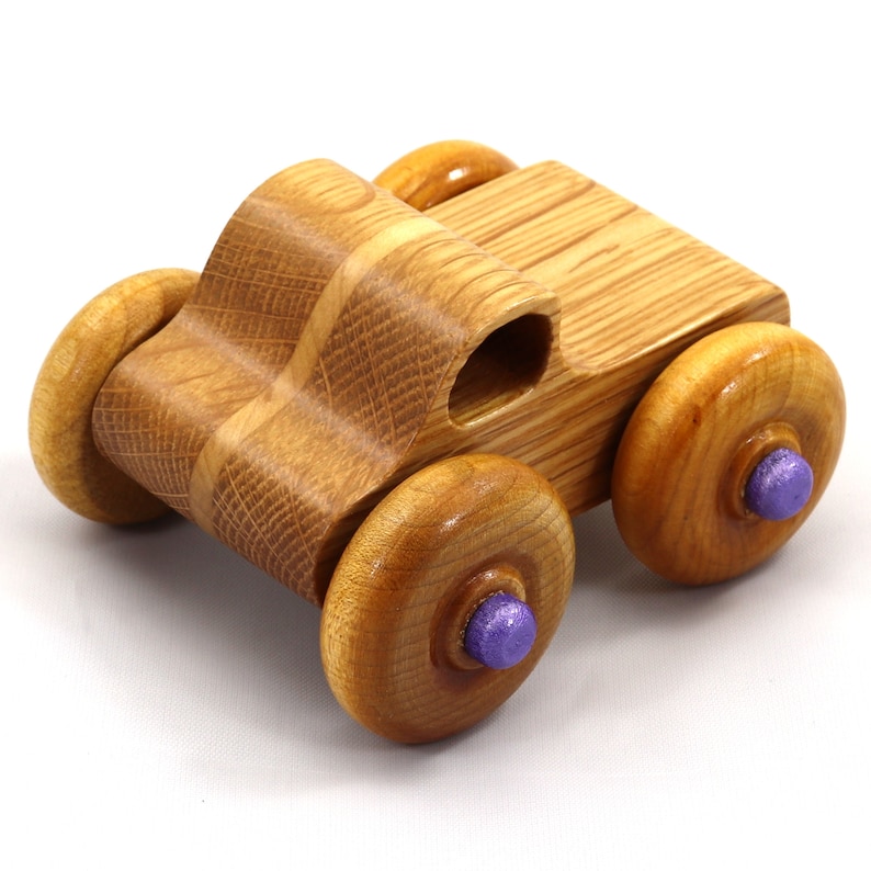 May include: A handcrafted wooden toy car with a natural wood finish. The car features four round wheels with purple center accents. The body of the car is a light brown color.