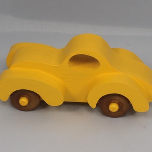 Handmade wooden toy car vintage style of a fat fendered coupe painted bright yellow with nonmarring amber shellac finished wheels. It is an excellent push toy for a younger child.