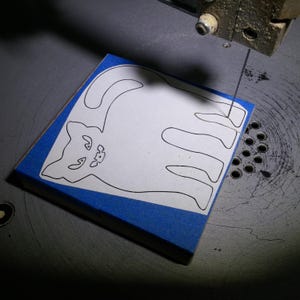 Unfinished wooden Halloween cat cutout pattern being hand-cut on a scroll saw in the toymaker's workshop.