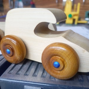Handmade wooden toy car. The body is finished with clear shellac, and the wheels are finished with amber shellac. The hubs are painted with metallic sapphire blue trim.