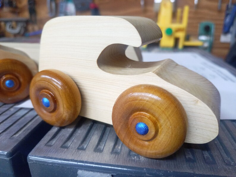 Handmade wooden toy car. The body is finished with clear shellac, and the wheels are finished with amber shellac. The hubs are painted with metallic sapphire blue trim.