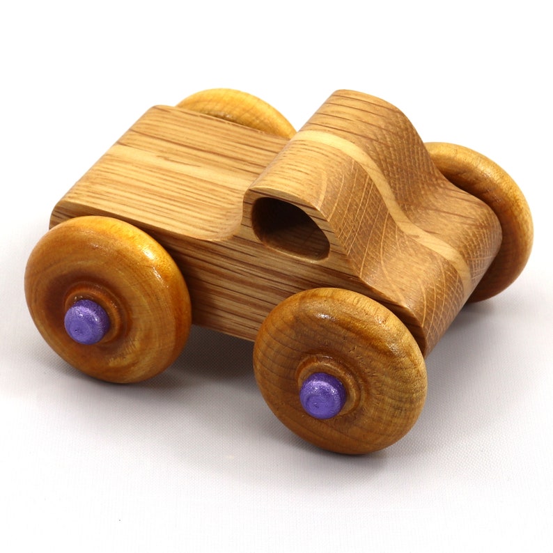 May include: A handcrafted wooden toy car with a natural wood finish. The car features four round wheels with purple centers. The body of the car has a curved design with a small opening. A classic toy for children.