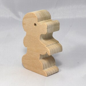May include: A wooden toy shaped like a standing animal with a hole in the top of its head. The toy is made of light brown wood and has a smooth, polished finish.