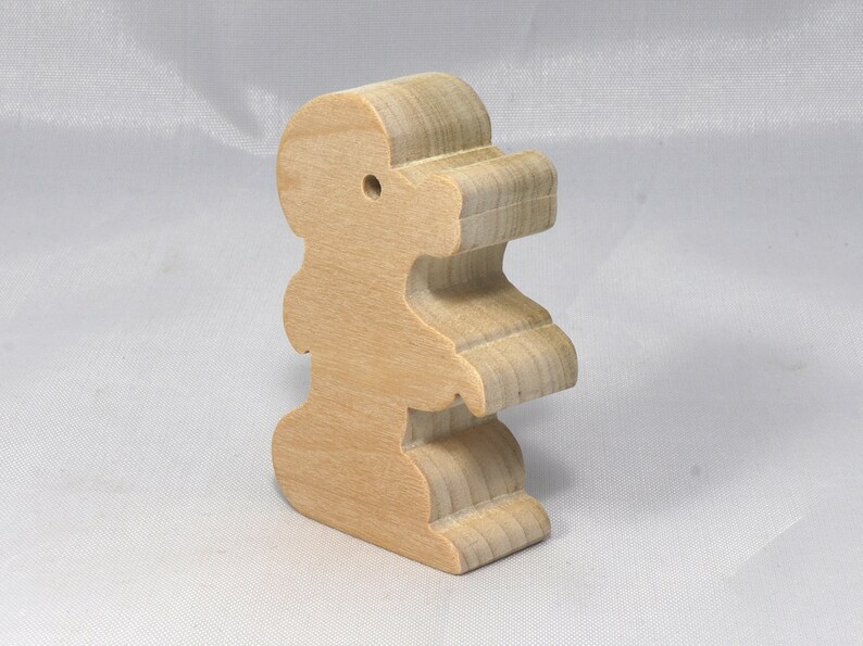May include: A wooden toy shaped like a standing animal with a hole in the top of its head. The toy is made of light brown wood and has a smooth, polished finish.