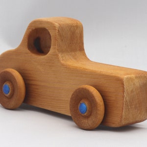 Wooden toy pickup truck from the Play Pal Collection at Odin's Toy Factory. Made from natural wood, finished with amber shellac, and accented with metallic sapphire blue acrylic paint on the wheel hubs. Made In The USA. Approximate dimensions: length 3-1/2 inches, height 1-3/8 inches, width 1-1/2 inches, wheels 3/4 inch diameter. Handmade in Tallahassee, Florida. Natural wood grain and color variations.