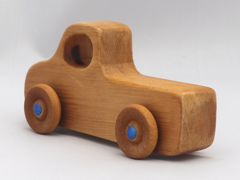 Wooden toy pickup truck from the Play Pal Collection at Odin's Toy Factory. Made from natural wood, finished with amber shellac, and accented with metallic sapphire blue acrylic paint on the wheel hubs. Made In The USA. Approximate dimensions: length 3-1/2 inches, height 1-3/8 inches, width 1-1/2 inches, wheels 3/4 inch diameter. Handmade in Tallahassee, Florida. Natural wood grain and color variations.