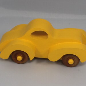 Handmade wooden toy car vintage style of a fat fendered coupe painted bright yellow with nonmarring amber shellac finished wheels. It is an excellent push toy for a younger child.