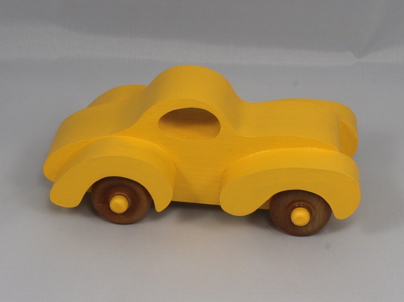 Handmade wooden toy car vintage style of a fat fendered coupe painted bright yellow with nonmarring amber shellac finished wheels. It is an excellent push toy for a younger child.
