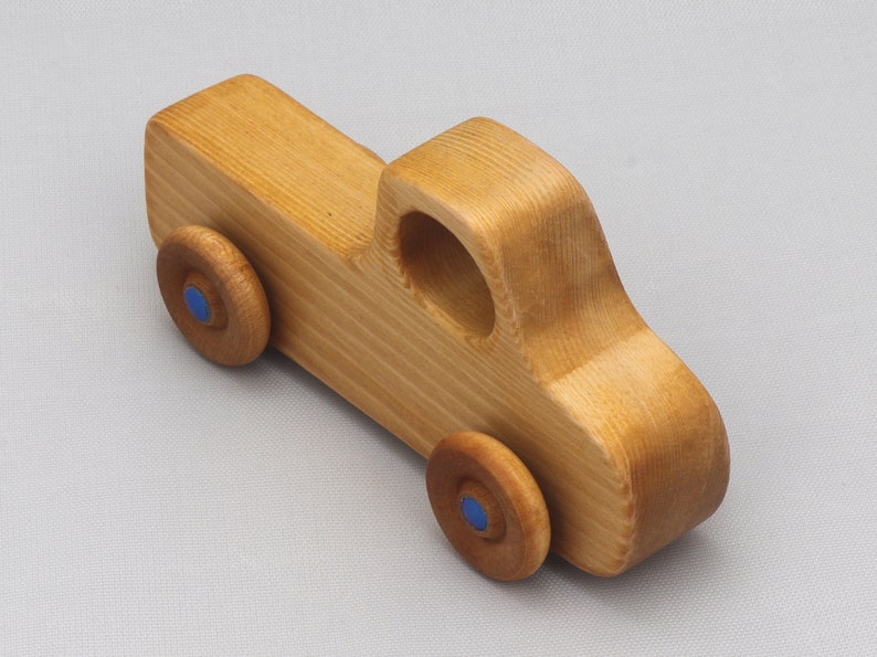 Wooden toy pickup truck from the Play Pal Collection at Odin's Toy Factory. Made from natural wood, finished with amber shellac, and accented with metallic sapphire blue acrylic paint on the wheel hubs. Made In The USA. Approximate dimensions: length 3-1/2 inches, height 1-3/8 inches, width 1-1/2 inches, wheels 3/4 inch diameter. Handmade in Tallahassee, Florida. Natural wood grain and color variations.