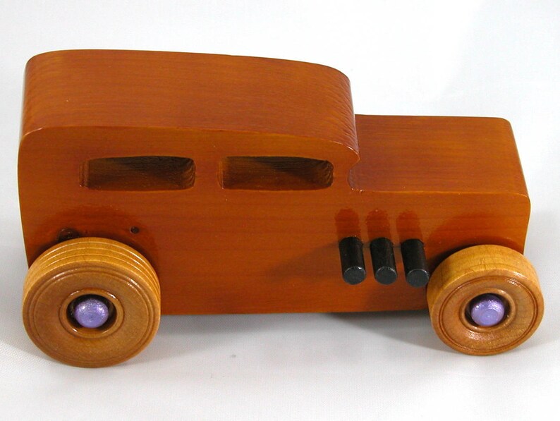 This is a handmade wooden toy car modeled after a Hot Rod 1932 Ford Sedan. It is made from wood, finished with multiple coats of amber shellac, and trimmed with black and metallic purple acrylic paint.