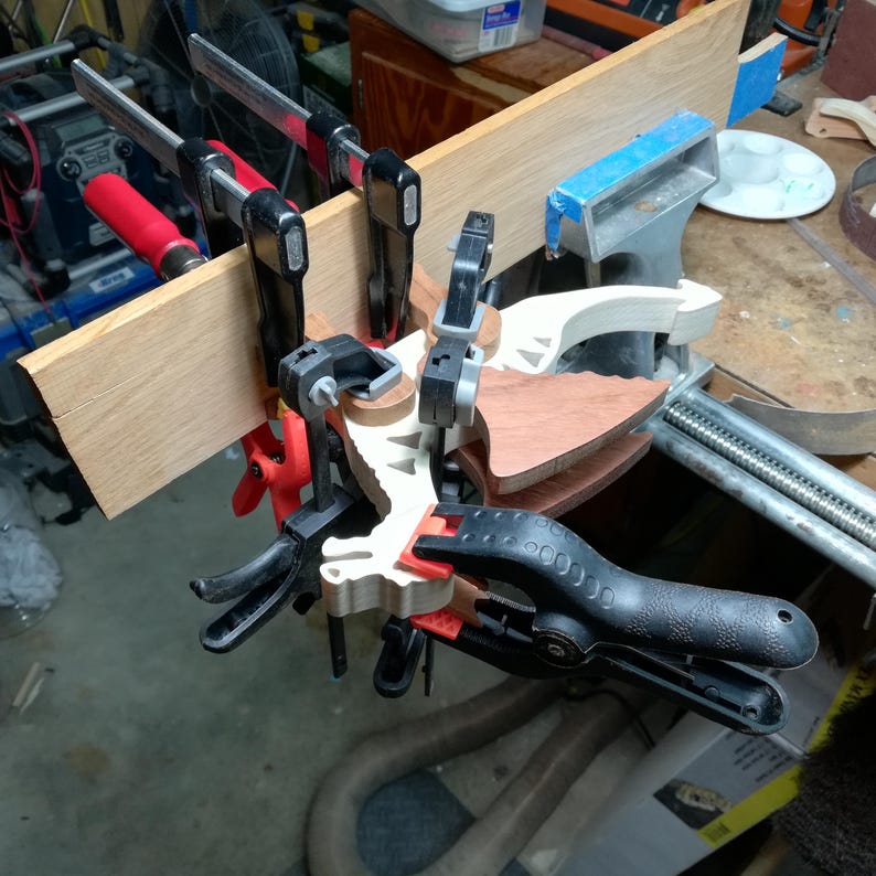 Wooden dragon under assembly in the workshop, held with several clamps beside a bench vise. The photo shows its light-colored body and tail, darker legs, and two wings positioned on either side.