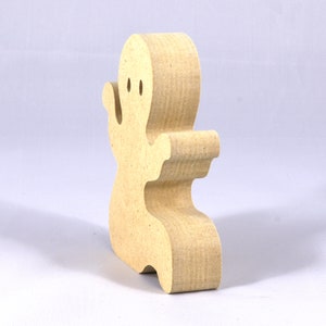 A handmade, unpainted wooden ghost cutout stands upright on a white background. The light-colored solid wood figure has a rounded head with two circular eye cutouts, raised wavy arms, and a curved wavy base, ready for painting or crafting.