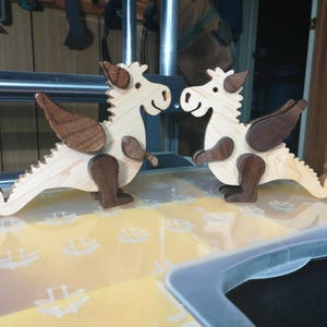Two handmade wooden baby dragon figurines with light hardwood bodies and dark contrasting parts facing each other in the woodworking shop.