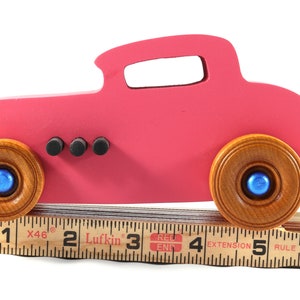 This is a handmade wooden Hot Rod '32 Deuce Coupe toy car. It is hand-painted hot pink with black and metallic sapphire blue trim. The hardwood wheels are finished with nonmarring amber shellac.