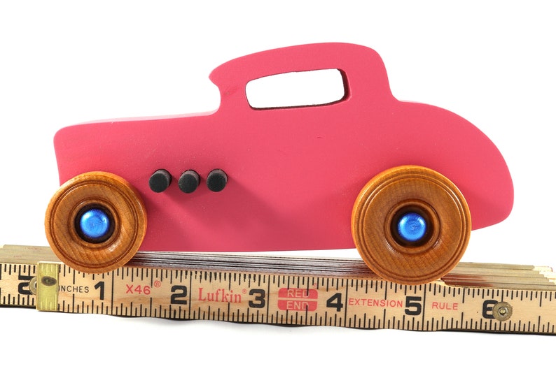 This is a handmade wooden Hot Rod '32 Deuce Coupe toy car. It is hand-painted hot pink with black and metallic sapphire blue trim. The hardwood wheels are finished with nonmarring amber shellac.