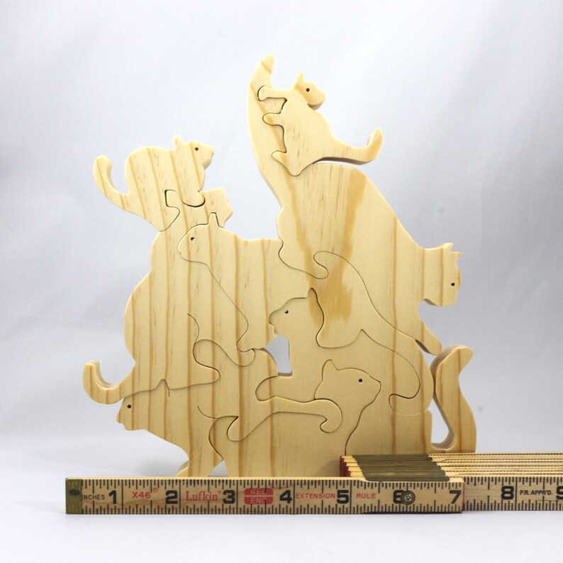 Handmade wooden puzzle featuring several cat-shaped pieces stacked on top of each other in various playful poses, forming a balanced tower. The cats are crafted with smooth edges and natural wood tones, highlighting their unique shapes and expressions.