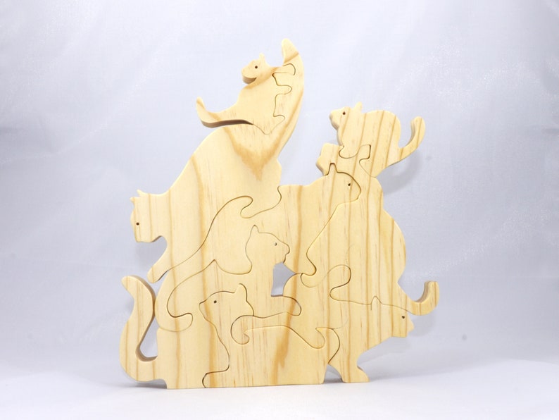 Handmade wooden puzzle featuring several cat-shaped pieces stacked on top of each other in various playful poses, forming a balanced tower. The cats are crafted with smooth edges and natural wood tones, highlighting their unique shapes and expressions.