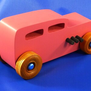 Handcrafted pink wooden hot rod '32 sedan toy car. Features black and metallic sapphire blue accents, and non-marking amber shellac wheels. Made to order for unique play or display.