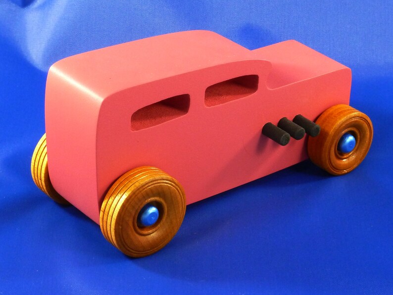 Handcrafted pink wooden hot rod '32 sedan toy car. Features black and metallic sapphire blue accents, and non-marking amber shellac wheels. Made to order for unique play or display.