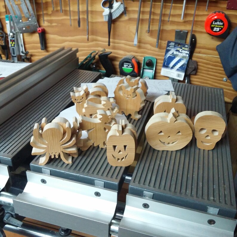 Handmade unfinished wooden Halloween cutouts displayed in a toymaker’s shop, including a skull, jack-o-lanterns, spider, cats, bat, and witch.