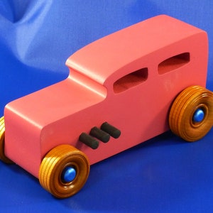 Handcrafted pink wooden hot rod '32 sedan toy car. Features black and metallic sapphire blue accents, and non-marking amber shellac wheels. Made to order for unique play or display.