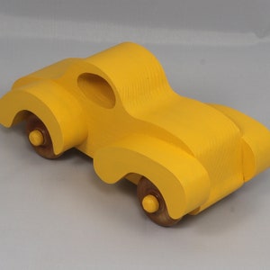 Handmade wooden toy car vintage style of a fat fendered coupe painted bright yellow with nonmarring amber shellac finished wheels. It is an excellent push toy for a younger child.
