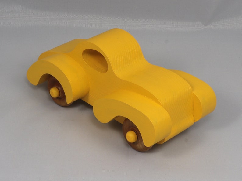 Handmade wooden toy car vintage style of a fat fendered coupe painted bright yellow with nonmarring amber shellac finished wheels. It is an excellent push toy for a younger child.