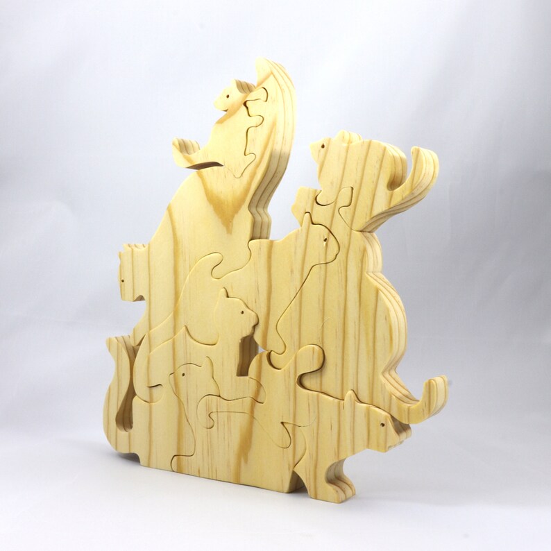 Handmade wooden puzzle featuring several cat-shaped pieces stacked on top of each other in various playful poses, forming a balanced tower. The cats are crafted with smooth edges and natural wood tones, highlighting their unique shapes and expressions.
