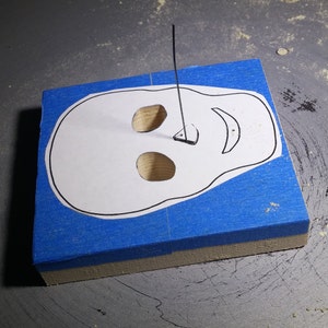 Expertly handcrafted from unfinished wood, this Halloween skull cutout displays detailed eye sockets, a nose, and a cheerful smile. Pictured during the scroll saw cutting.