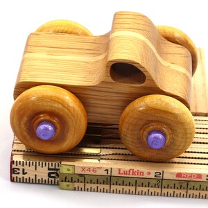 May include: A handcrafted wooden toy truck with four large, round wheels. The wheels have purple centers. The truck is made of light-colored wood and sits on a vintage measuring tape.