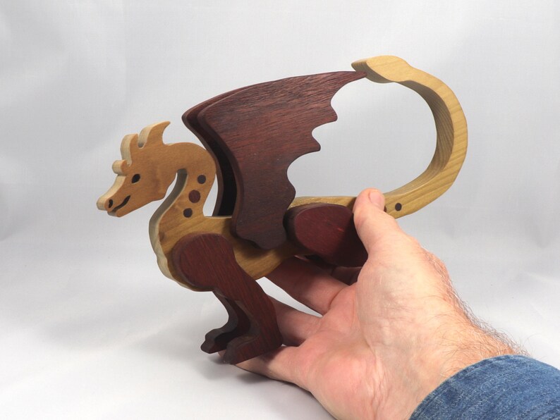 Handmade wood dragon figurine made from select grade contrasting hardwoods and hand-finished with a custom mixture of mineral oil and waxes. Displayed in the makers hand for scale.