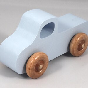 May include: A light blue wooden toy truck with natural wood wheels. The truck has a classic pickup design with a cab and a cargo bed. The wheels are round and attached to the truck's body.