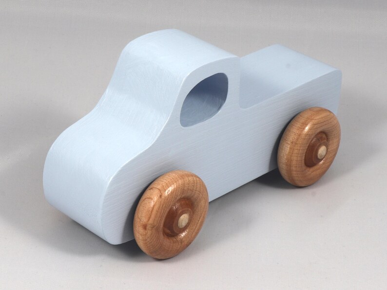 May include: A light blue wooden toy truck with natural wood wheels. The truck has a classic pickup design with a cab and a cargo bed. The wheels are round and attached to the truck's body.