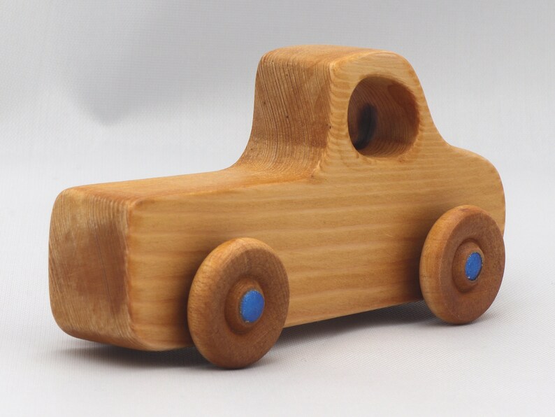 Wooden toy pickup truck from the Play Pal Collection at Odin's Toy Factory. Made from natural wood, finished with amber shellac, and accented with metallic sapphire blue acrylic paint on the wheel hubs. Made In The USA. Approximate dimensions: length 3-1/2 inches, height 1-3/8 inches, width 1-1/2 inches, wheels 3/4 inch diameter. Handmade in Tallahassee, Florida. Natural wood grain and color variations.