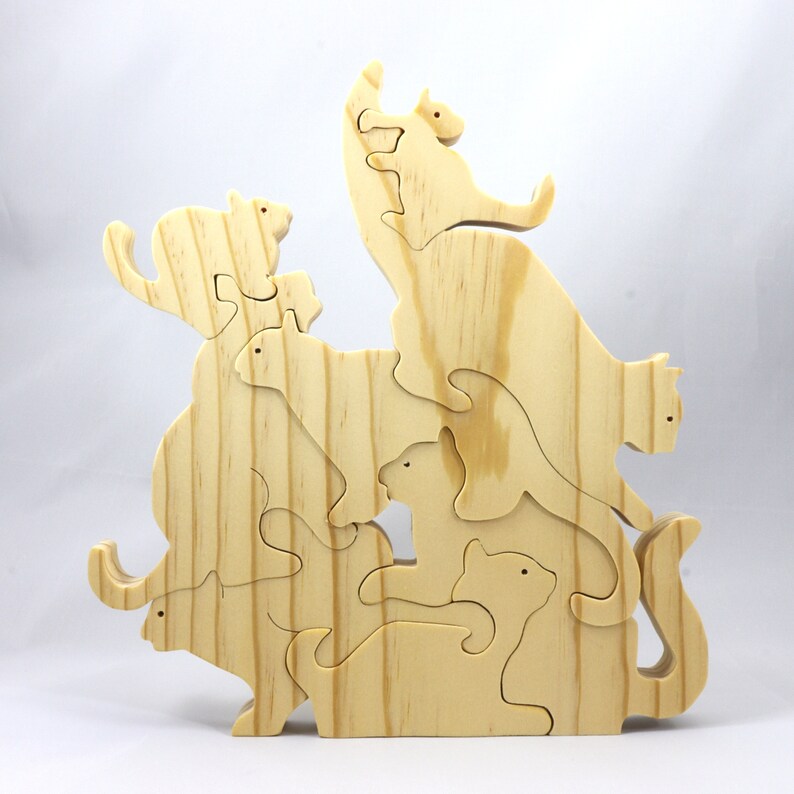 Handmade wooden puzzle featuring several cat-shaped pieces stacked on top of each other in various playful poses, forming a balanced tower. The cats are crafted with smooth edges and natural wood tones, highlighting their unique shapes and expressions.