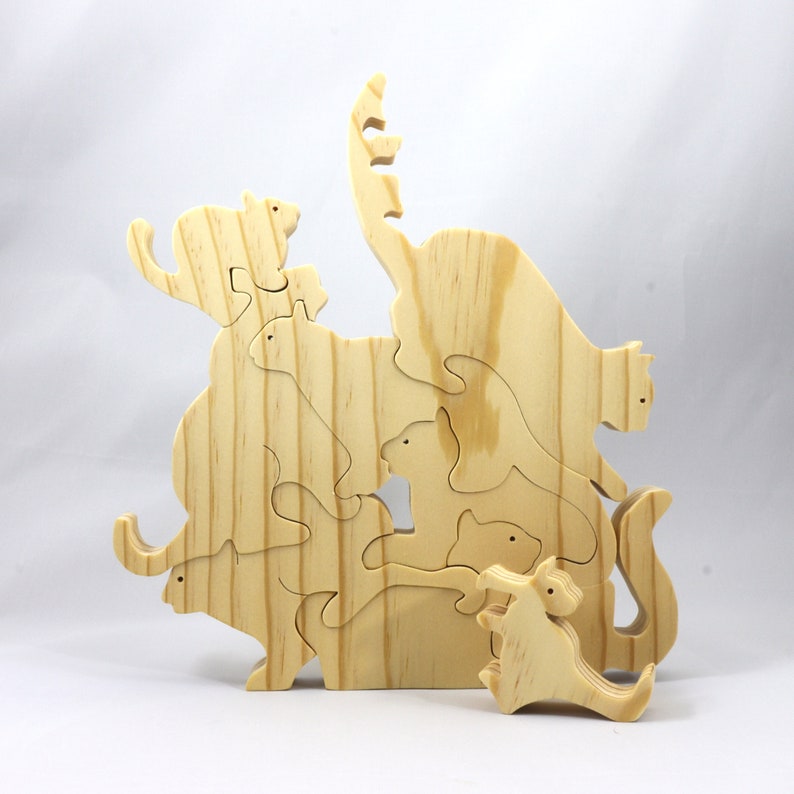 Handmade wooden puzzle featuring several cat-shaped pieces stacked on top of each other in various playful poses, forming a balanced tower. The cats are crafted with smooth edges and natural wood tones, highlighting their unique shapes and expressions.