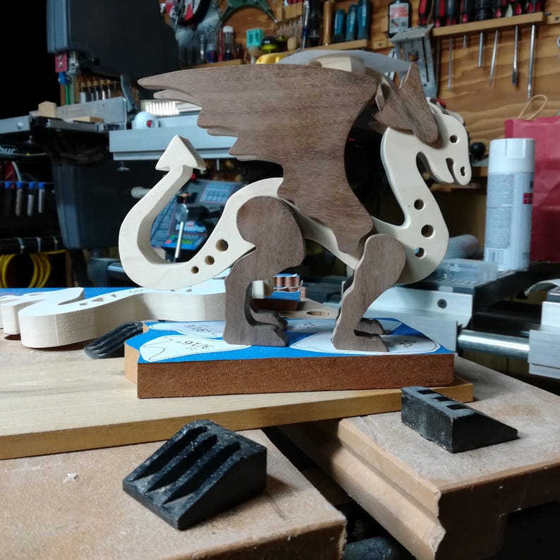Handmade wooden dragon figurine made from contrasting hardwoods with a light natural wood body and head paired with rich dark reddish-brown wings, legs, and horns. Displayed in my shop prior to finishing.