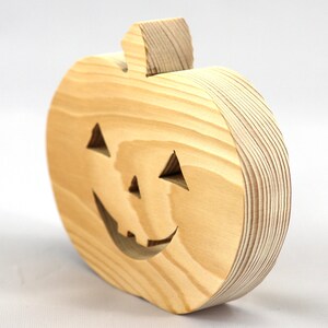 Handmade unpainted wooden Jack-o-Lantern cutout with carved triangular eyes, nose, smiling mouth, and stem, shown freestanding on a white background. Ready to paint for Halloween decoration.