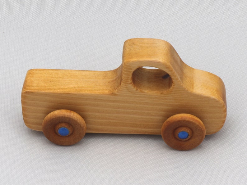 Wooden toy pickup truck from the Play Pal Collection at Odin's Toy Factory. Made from natural wood, finished with amber shellac, and accented with metallic sapphire blue acrylic paint on the wheel hubs. Made In The USA. Approximate dimensions: length 3-1/2 inches, height 1-3/8 inches, width 1-1/2 inches, wheels 3/4 inch diameter. Handmade in Tallahassee, Florida. Natural wood grain and color variations.
