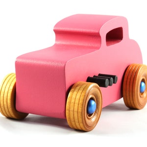 This is a handmade wooden Hot Rod '32 Deuce Coupe toy car. It is hand-painted hot pink with black and metallic sapphire blue trim. The hardwood wheels are finished with nonmarring amber shellac.